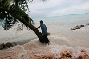Pita Meanke, de la aldea de Betio, se para junto a un árbol mientras observa cómo las 'mareas reales' atraviesan el malecón de su familia y el mar se derrama sobre su propiedad familiar, en la isla de Kiribati, en el Pacífico Sur.